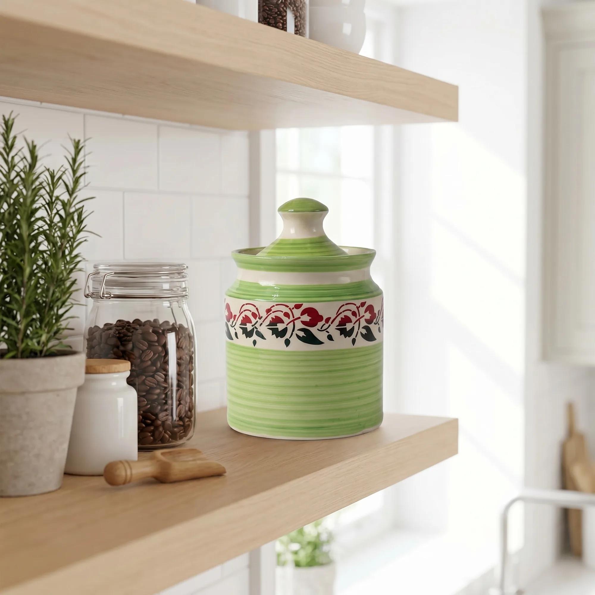 Green floral ceramic storage jar with lid placed on a light wooden floating shelf in a modern kitchen setting.