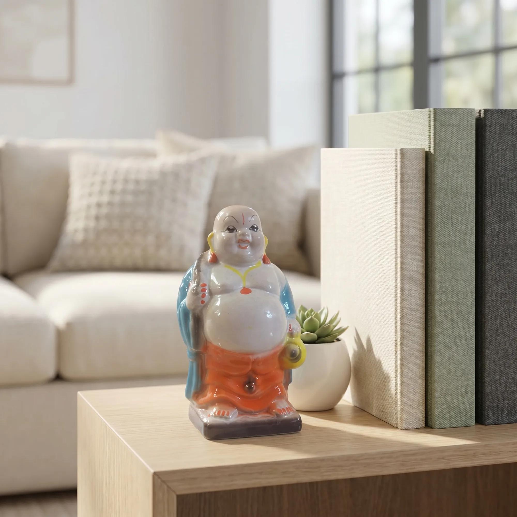 Ceramic Laughing Buddha idol with orange and blue accents, placed on a light wooden table in a modern living room setting.