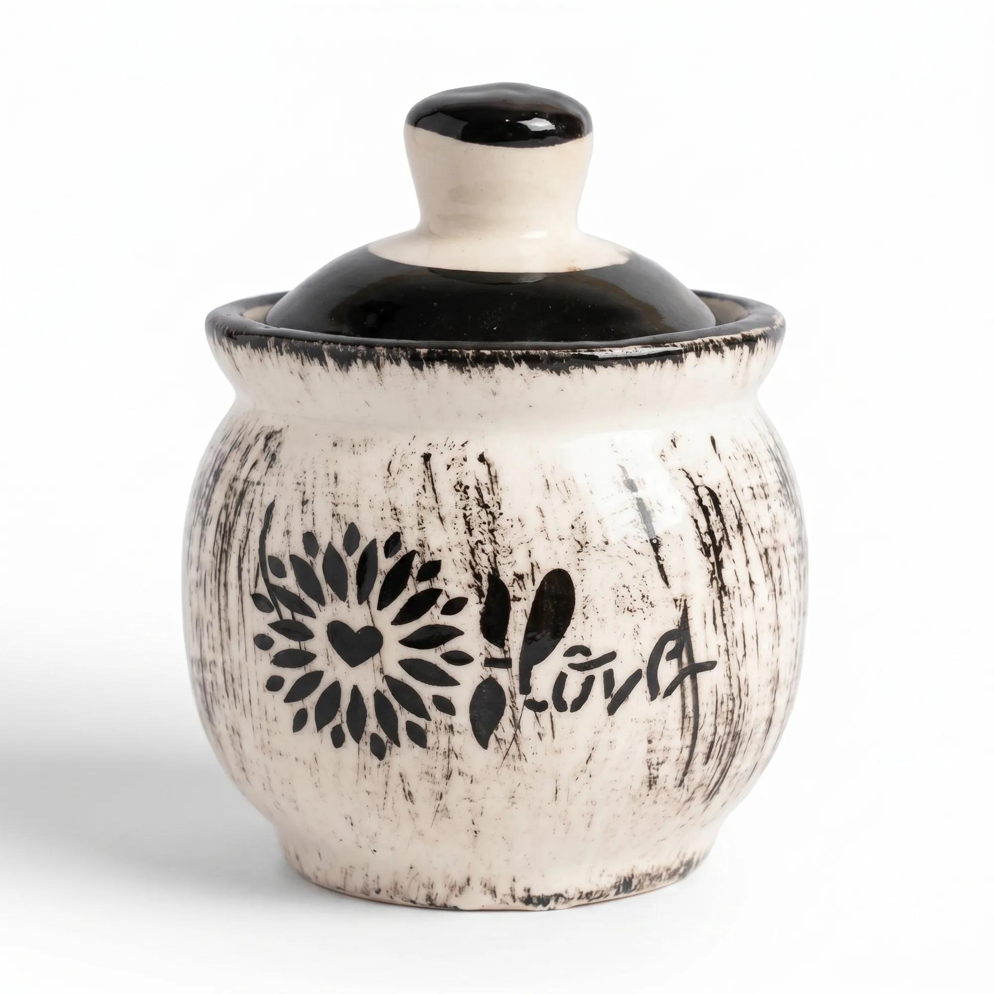 A front view of the small, round 100ml white ceramic storage jar with a black floral pattern and matching lid on a white background.